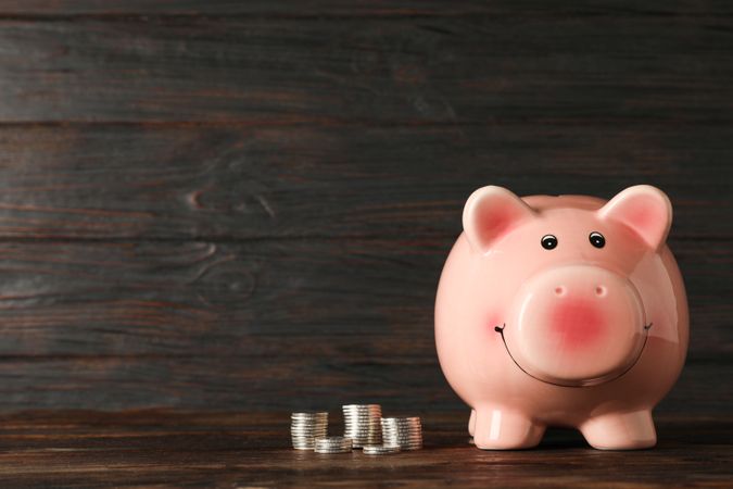 Happy piggy bank with money on wood table against wooden background, space for text. Finance, saving money