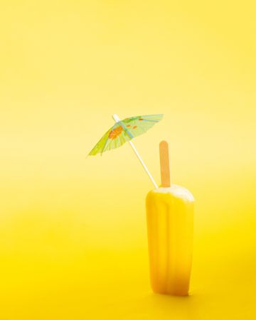 Ice pop with cocktail parasol on yellow background