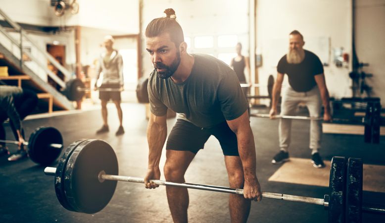 Focused man performing deadlifts in busy gym