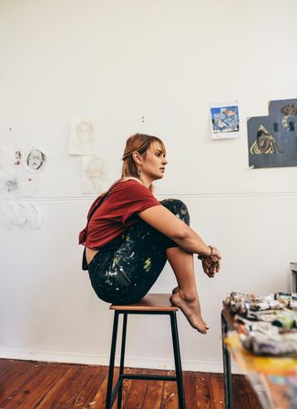Side view of woman sitting on stool in her art studio