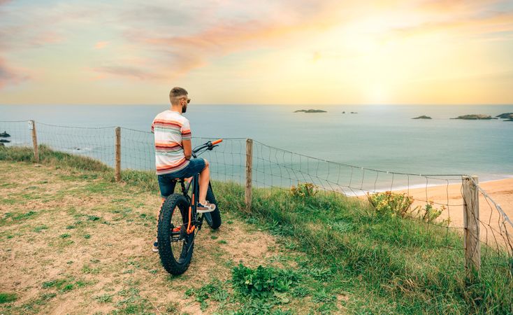 Male standing with bicycle looking down at beautiful ocean view