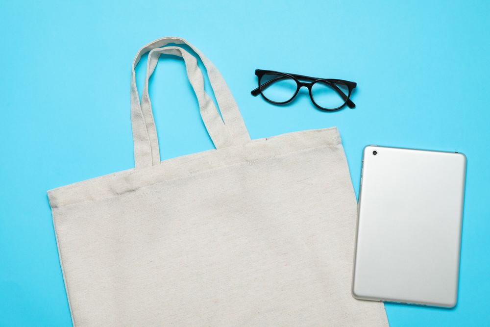 Eco bag, tablet and glasses on color background, space for text