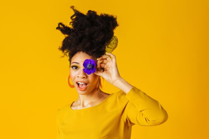 Surprised Black woman sticking her tongue out with one purple flower over her eye