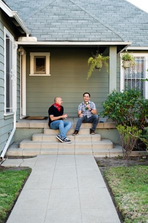 Two men talking and having a beer while sitting on front porch of house