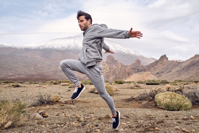 Young positive man in activewear jumping on rocky terrain