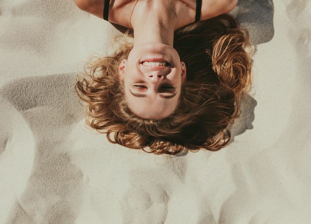 Close up of a smiling woman lying on beach sand on a sunny day