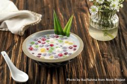Thai dessert of colorful rice balls in sweet coconut milk on wooden table 0KdEM5