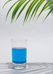 Side view of cold blue drink in glass under green palm branch