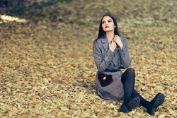 Content female sitting relaxing in park in fall time with colorful leaves on ground