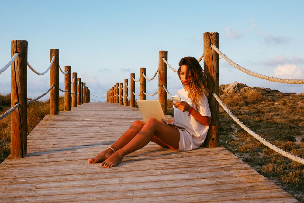 Woman using laptop and mobile phone sitting on bridge