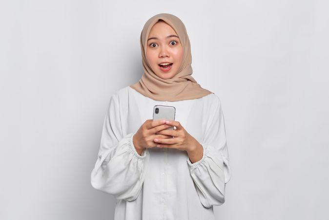 Amazed Asian female in headscarf looking up from cell phone