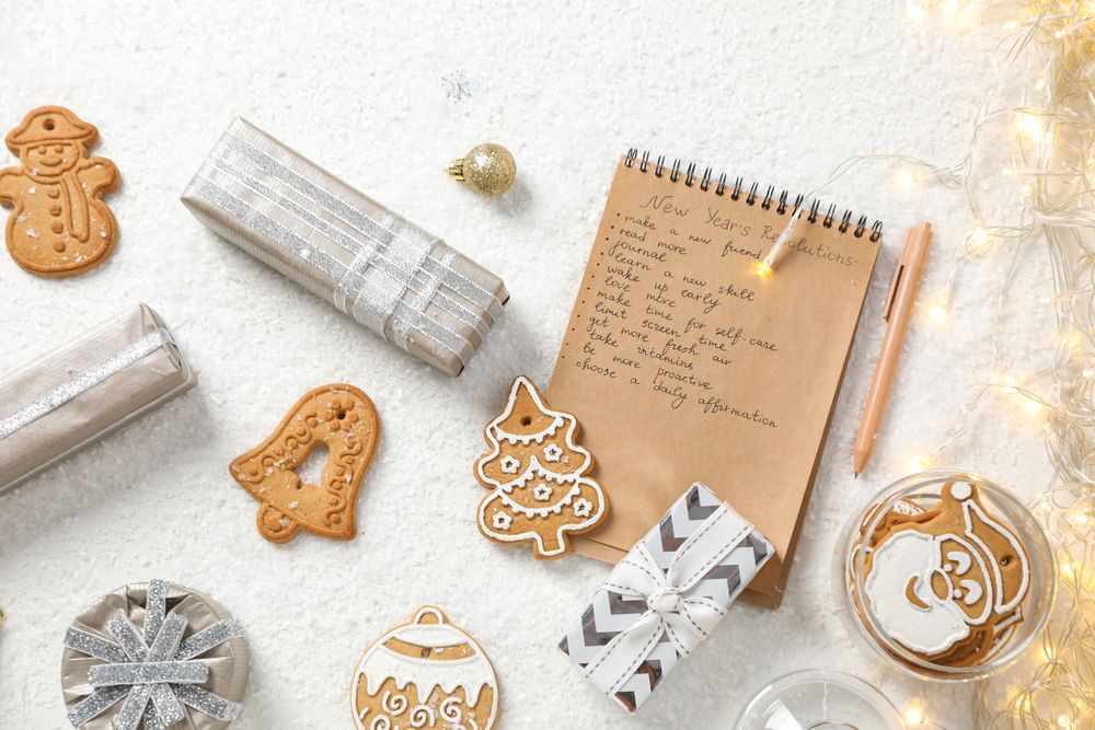 Cookies, gift boxes and notepad with list on plain background, top view