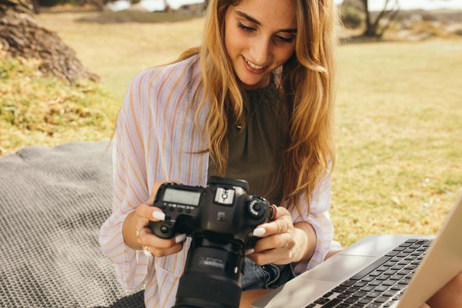 Close up of woman photographer sitting outdoors holding a dslr camera and laptop computer
