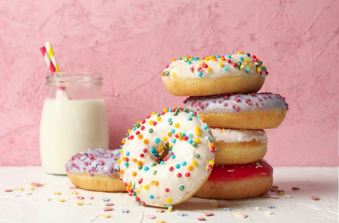 Milk and tasty donuts against pink background