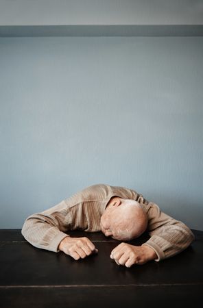 Exhausted man feeling headache and negative emotions while sitting at the table