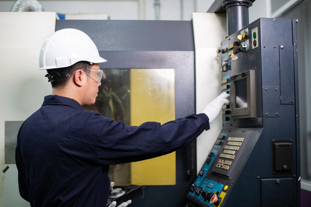Man operating controls in factory in safety helmet and coveralls