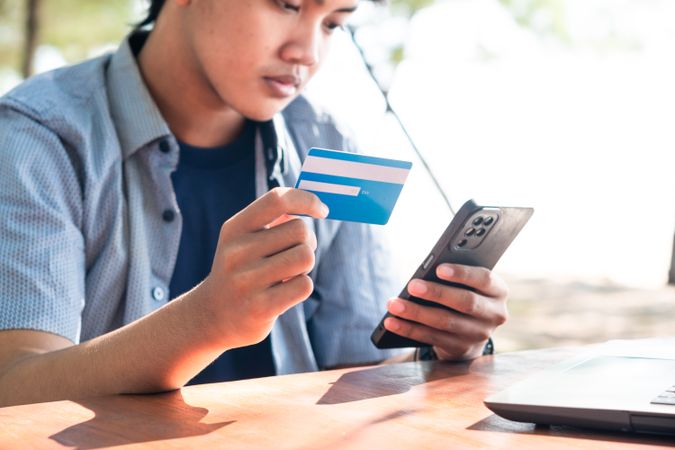 Happy Asian Young businessman hold blue creditcard and phone purchasing online shopping in outdoor cafe.