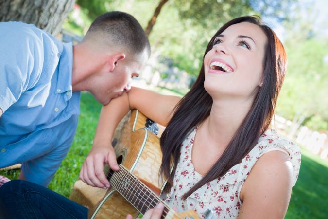Young Adult Female Playing Guitar with Partner In The Park.