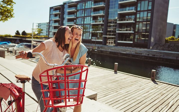 Two close friends laughing while walking and talking along the waterfront, copy space