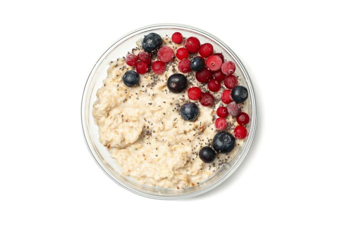Bowl with oatmeal porridge and ingredients isolated on plain background