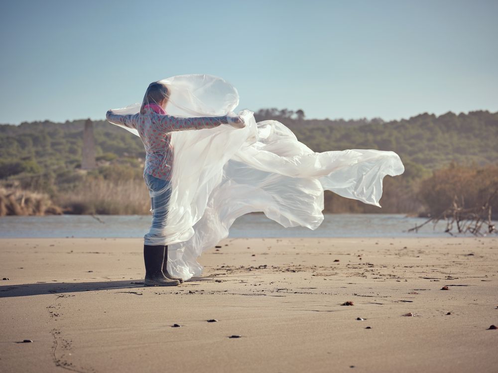 Girl caught up in plastic sheet standing on sandy shore