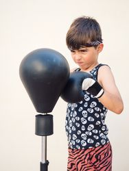 Sporty boy in boxing gloves beating punch bag