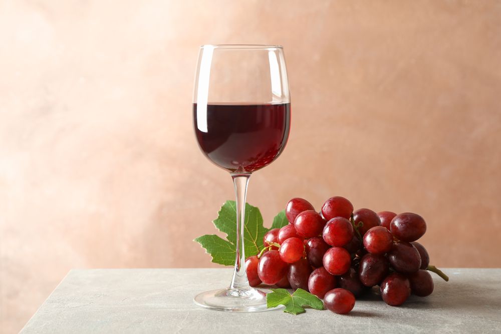 Grape and glass with wine on grey background, space for text