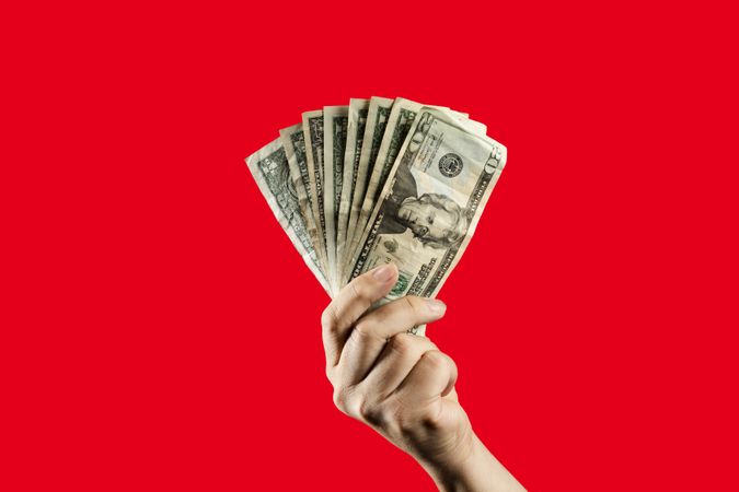 Hand holding a fan of US dollar bills against a vibrant red background.