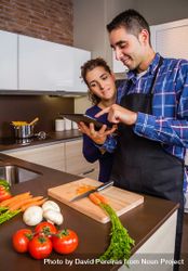 Couple reading digital tablet for instruction while prepping dinner 5zJNA5