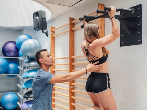 Trainer helping fit female with pull ups