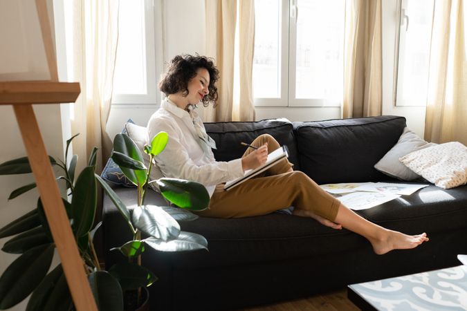 Woman writing on paper on sofa in room