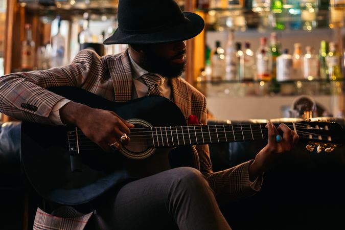 Stylish Black man in classic outfit playing guitar