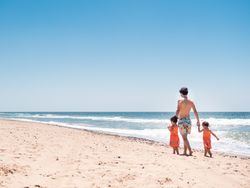 Father walking on sandy beach with toddler daughters