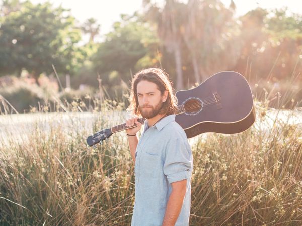 Hipster man in jungle with guitar