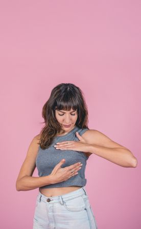 Woman doing a Breast Self-Exam checking up breast changes over pink background. Copy space