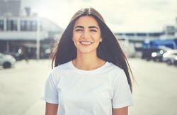 Smiling woman with long straight brown hair outside on street with parked cars