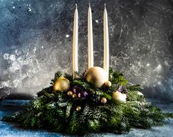Side view of Christmas festive center piece of long candles surrounded by baubles in pine branches