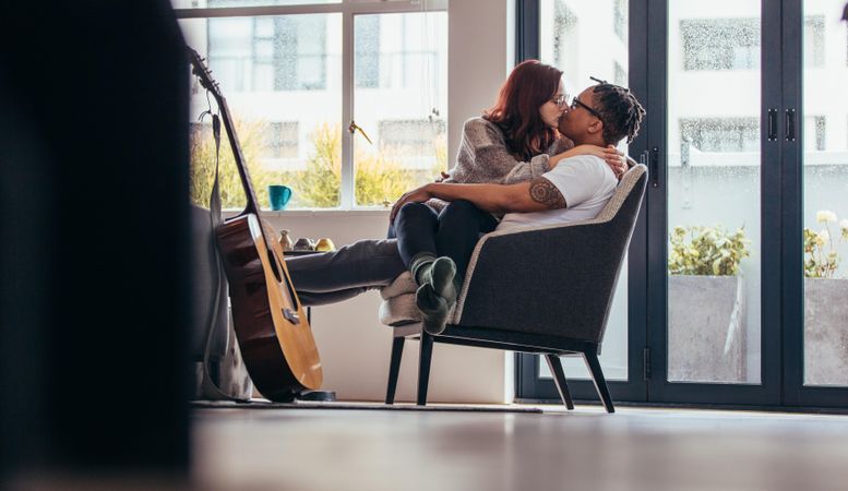 Interracial couple sitting on a armchair and kiss one another