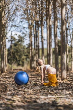 Adult pregnant woman training with pilates ball in park during sunny day
