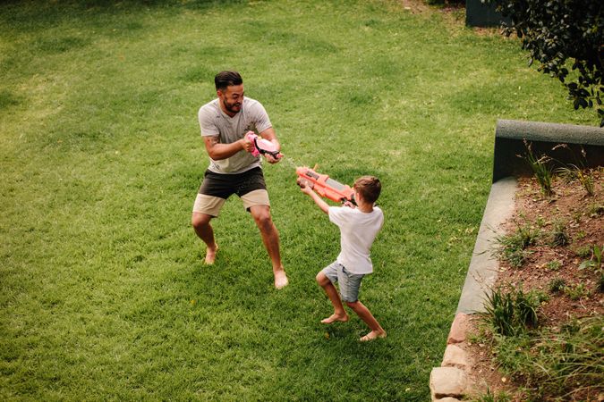 Boy playing water guns with father in backyard lawn