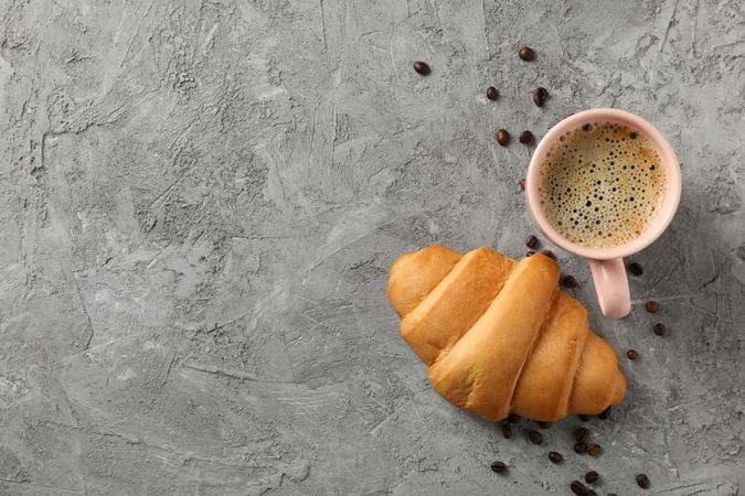 Croissant and pink mug of coffee on grey table, top view, copy space