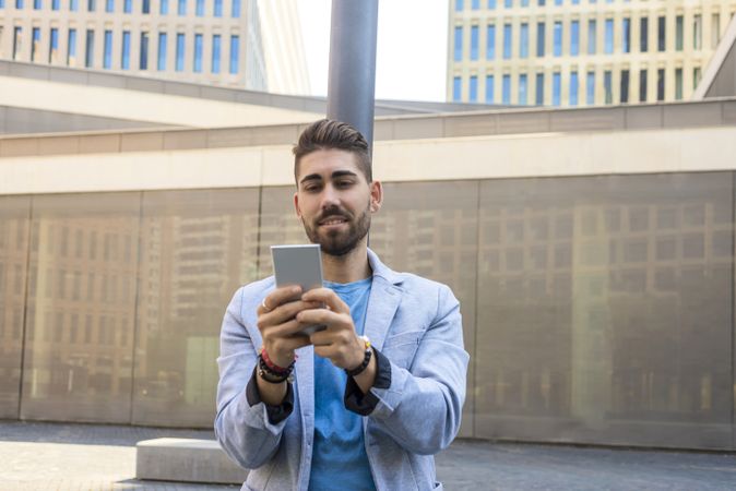 Smiling man in blazer leaning on pole outside talking on video call