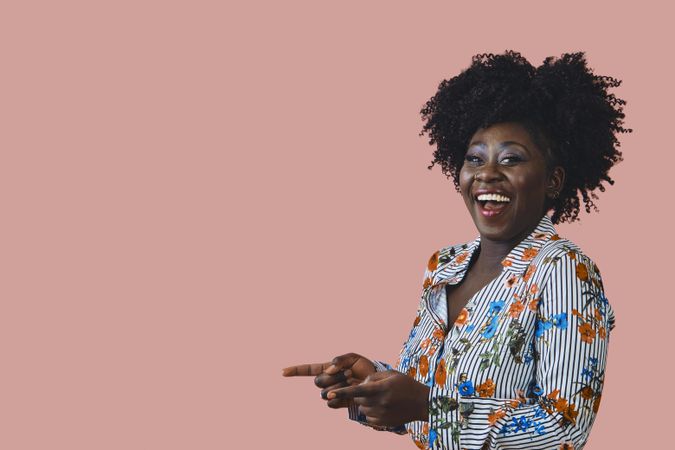 Studio shot of a cheerful and confident Black woman in floral print shirt pointing her fingers