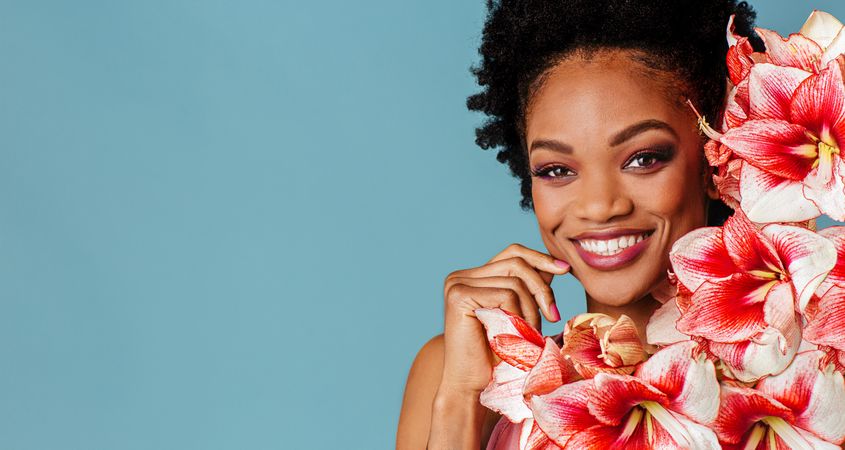 Studio shoot of smiling Black woman surrounded by flowers with copy space