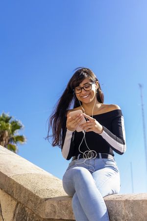 Young smiling woman with eyeglasses chatting on mobile phone while sitting outdoors