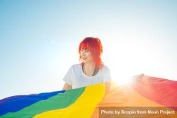 Young woman with red hair holding rainbow flag under blue sky 49Egm4