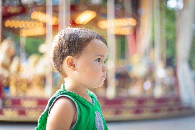 Child looking away against moving carousel at fair