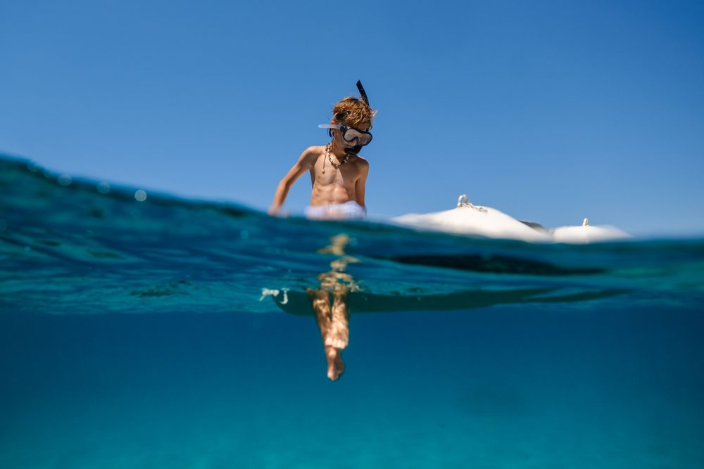 Boy in snorkeling mask floating on board of boat in sea
