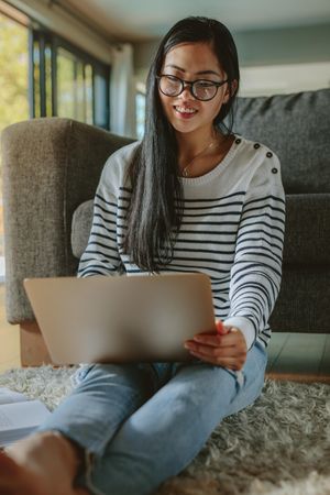 Woman sitting on floor and leaning to sofa using laptop