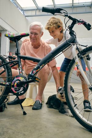 Smiling boy hugging grandfather fixing bicycle